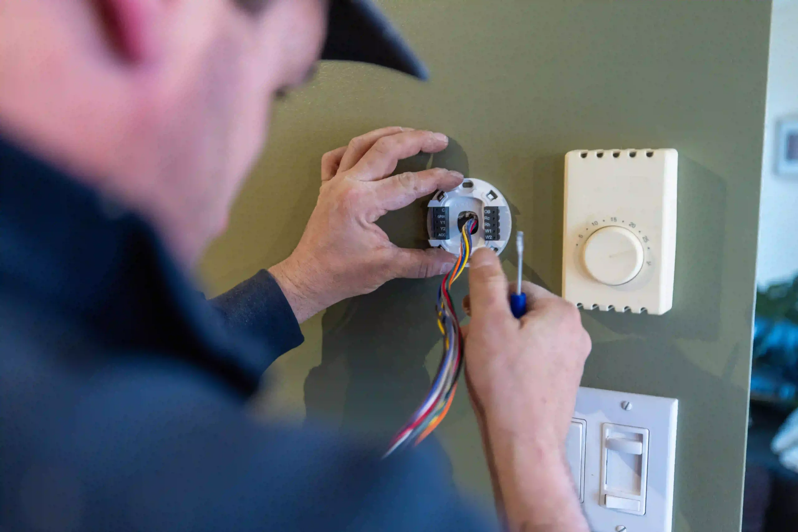 Technicien branchant un thermostat mural pour un système de chauffage et climatisation résidentiel